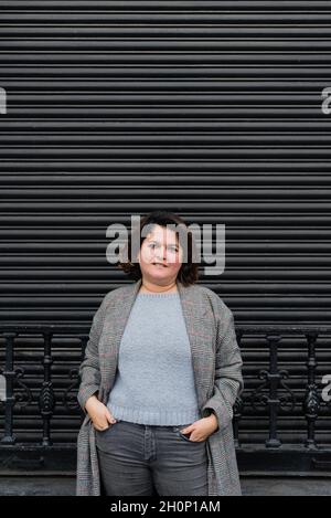 Vertical portrait of a woman, wearing a long gray-scale jacket, smiling at the camera and holding her hands in her pockets. Copy space Stock Photo