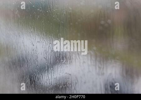 Rainy day through the window on cloudy grey sky and city buildings background. Concept. Evening cityscape behind the glass window with trickling drops Stock Photo