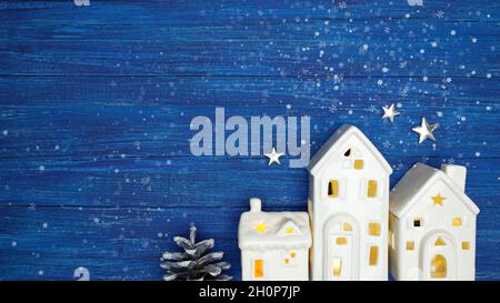 christmas and new year background. little toy christmas houses with a burning light inside, silver stars and pine cone on blue rustic planks Stock Photo