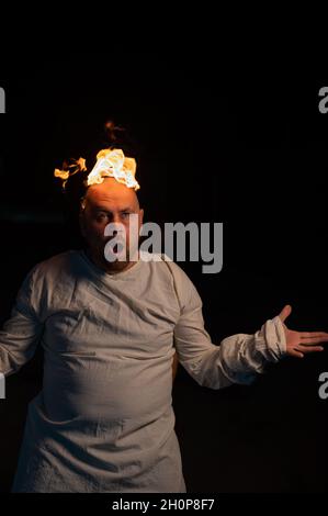 Bald man in a straitjacket with a burning head on a dark background. Stock Photo