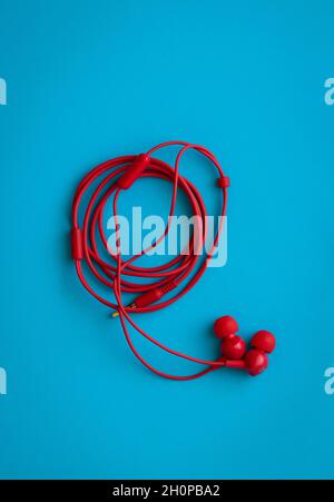 Red headphones with rolled wire, on a blue blbackground Stock Photo