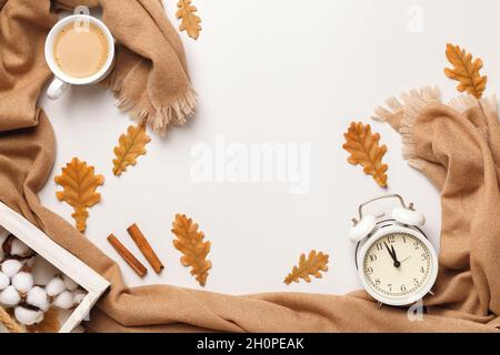 Autumnal cosiness concept. Beige cashmere scarf coffee cup alarm clock with autumn oak leaves on a light gray background. Flat lay top view copy space Stock Photo
