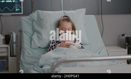 Portrait of tired sick child sleeping after suffering medical recovery surgery during disease examination in hospital ward. Hospitalized kid resting in bed wearing oxygen nasal tube Stock Photo