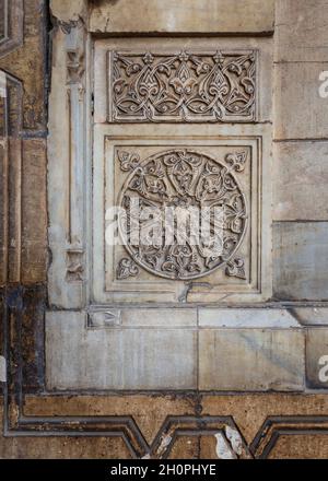 Round floral patterns framed by geometrical patterns carved into the exterior ancient stone wall of Sultan Hasan Mosque, Old Cairo, Egypt Stock Photo