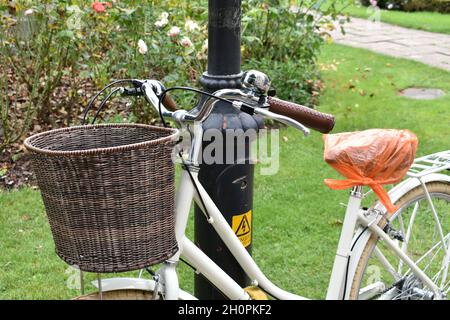 close up of lady's bicycle leaning against a lamppost in public park.  Woman's bike with basket on the front by handlebars Stock Photo