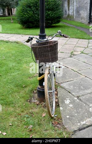 close up of lady's bicycle leaning against a lamppost in public park.  Woman's bike with basket on the front by handlebars Stock Photo