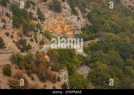 Road autumn forest aerial. Beautiful view of the colorful orange-brown forest in the sunset warm light. A winding road along a mountain serpentine wit Stock Photo