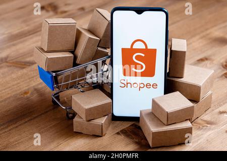 Shopee is e-commerce technology company. Smartphone with Shopee logo on the screen, shopping cart and parcels. Stock Photo