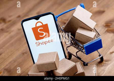 Shopee is e-commerce technology company. Smartphone with Shopee logo on the screen, shopping cart and parcels. Stock Photo