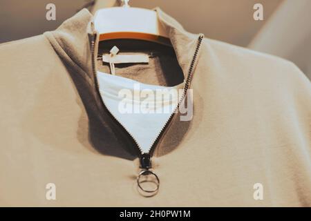 A set of a white T-shirt and a beige polo with a zipper collar hangs on a white hanger in a clothing store. Casual clothes. Shopping. Stock Photo