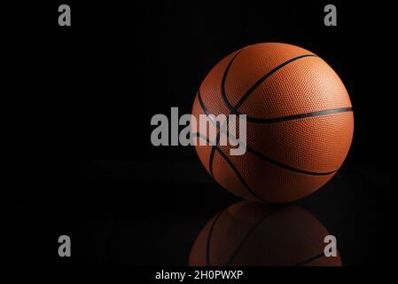 Closeup shot of a brown basketball ball with black stripes on a black background with a reflection Stock Photo