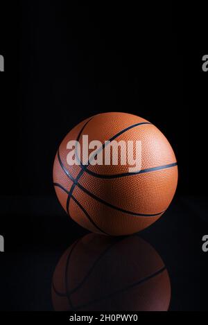Vertical closeup shot of a brown basketball ball with lines on a black background with a reflection Stock Photo