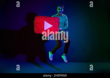 Full length body size photo man in sunglass jumping with streaming service icon isolated on dark blue color background Stock Photo