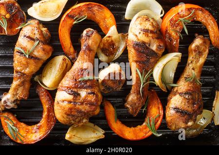 Black grill background with chicken legs, pumpkin slices, onion and garlic close-up. Horizontal top view from above Stock Photo