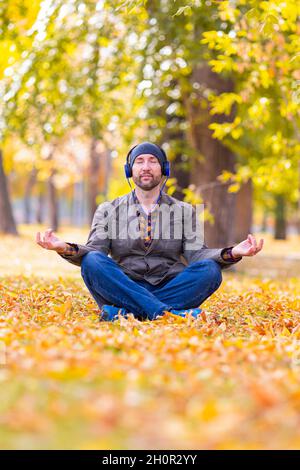 Relaxed middle aged bearded Caucasian man in sitting in lotus pose in city park. Confident middle aged businessman resting in autumn park. Tranquility Stock Photo