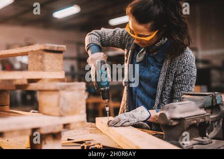 Female carpenter using drill while working in workshop. Female doing male's work concept. Stock Photo