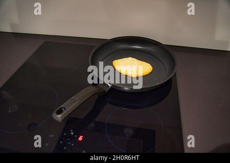 Food being cooked on a black hot frying pan on the modern stove in the kitchen Stock Photo