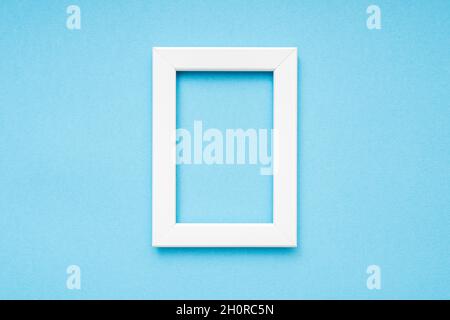 White wooden photo frame on blue surface, minimal composition, Vertical photo frame, space for text, top view Stock Photo