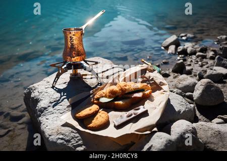 Copper Cezve with coffee on a gas stove in autumn lake camping in the mountains. Preparing coffee outdoor concept Stock Photo