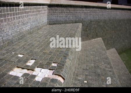 Missing tiles in a grey mosaic abandoned swimming pool Stock Photo