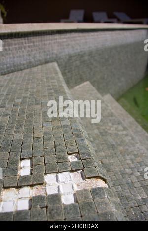 Missing tiles in a grey mosaic abandoned swimming pool Stock Photo