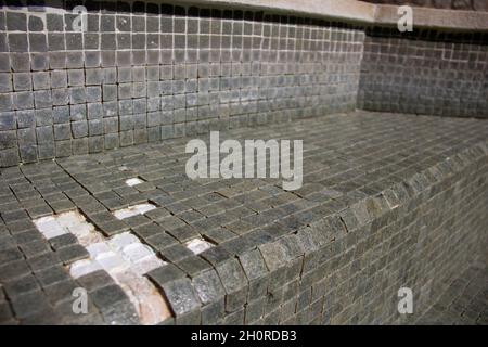 Missing tiles in a grey mosaic abandoned swimming pool Stock Photo