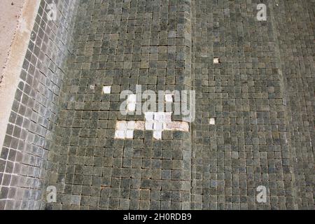 Missing tiles in a grey mosaic abandoned swimming pool Stock Photo