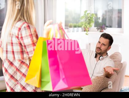 Portrait of young man sitting on sofa, listening music and feeling upset because his girlfriend was in shopping again Stock Photo