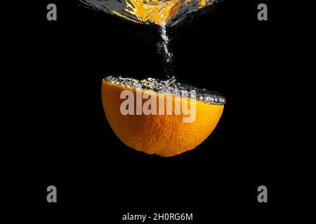 Fresh sliced orange fruit in water splash isolated on black background. Minimal food concept. Stock Photo