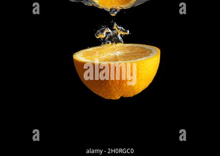 Fresh sliced orange fruit in water splash isolated on black background. Minimal food concept. Stock Photo