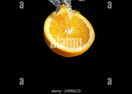 Fresh sliced orange fruit in water splash isolated on black background. Minimal food concept. Stock Photo