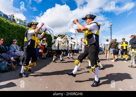 Two Rows of Wantsum Morris men dancing outdoors holding white handkerchiefs in their hands at Broadstairs Folk week festival. Sunshine, blue sky. Stock Photo