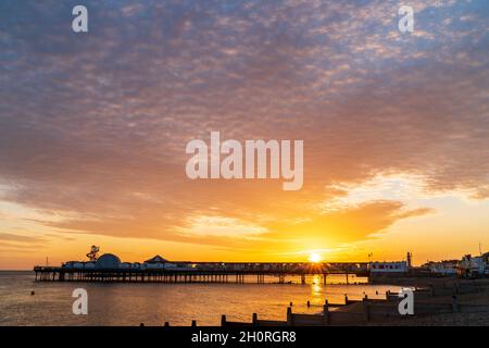Sunrise over a Victorian pier at the resort town of Herne Bay on the Kent Coast in England. Sky filled altocumulus under-lit by the rising sun. Stock Photo