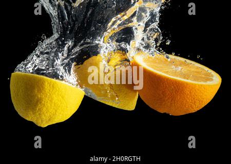 Fresh sliced orange and lemon in water splash isolated on black background. Minimal food concept. Stock Photo