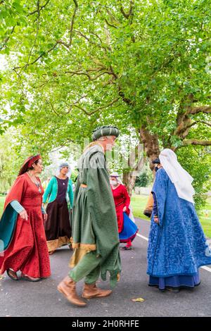 Group of Medieval re-enactors dancing on a footpath under some trees. Four women and two men dressed in colourful medieval costume. Stock Photo