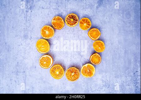 Minimalist Christmas wreath or Advent crown: dried orange slices in bright colors, arranged in a circle on a background with concrete look. Stock Photo