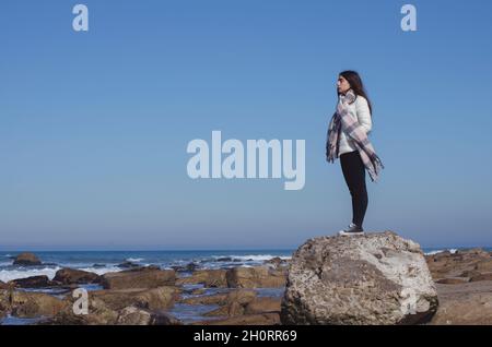 Teenage girl standing on a rock looking at view, Mar del Plata, Buenos Aires Province, Argentina Stock Photo