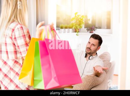 Portrait of young man sitting on sofa, listening music and feeling upset because his girlfriend was in shopping again Stock Photo