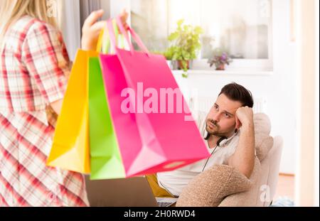 Portrait of young man sitting on sofa, listening music and feeling upset because his girlfriend was in shopping again Stock Photo