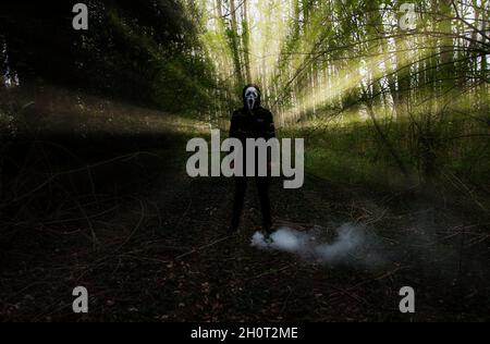 scary man standing in the woods with a white mask. Stock Photo