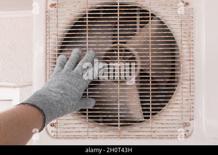 The hand of an air conditioner repair and maintenance specialist in a construction glove working with air-conditioned old equipment. Stock Photo