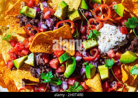 Mexican food concept. Corn nachos chips with avocado, pepper, salsa and grilled minced beef, close-up, top view. Stock Photo