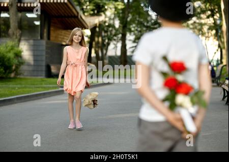 Children's date, boy hides flowers from a girl Stock Photo