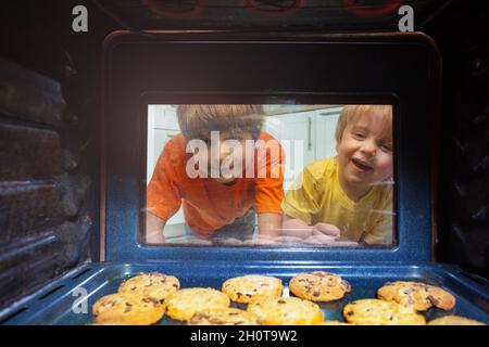 Curious kids look though oven glass at cookies Stock Photo