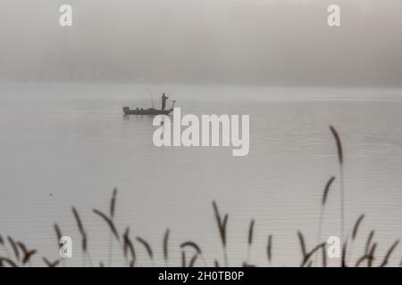Plainwell, Michigan - A man fishes from a boat on Pine Lake in the early morning fog. Stock Photo