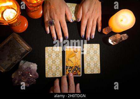 Detail of a woman's hands showing three tarot cards on a table of black cards, while another hand shows the card of death as the chosen one. Concept o Stock Photo