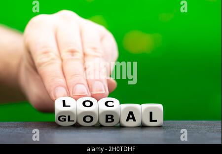Hand turns dice and changes the word global to local. Stock Photo