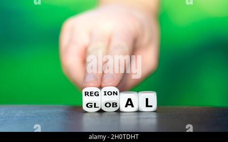 Hand turns dice and changes the word global to regional. Stock Photo