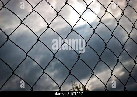 Metal mesh-netting against the background of a stormy sky. Disturbing abstract background. Chain-link mesh texture. Stock Photo