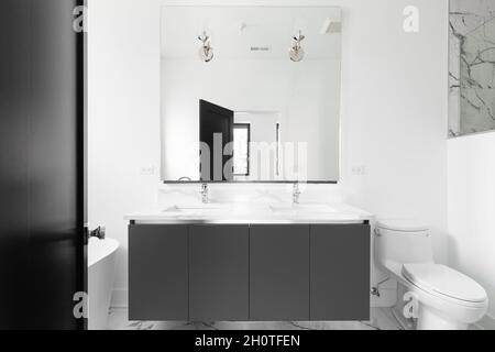 A luxurious bathroom with a grey vanity cabinet, white marble countertop, lights mounted on the mirror, and a black door. Stock Photo